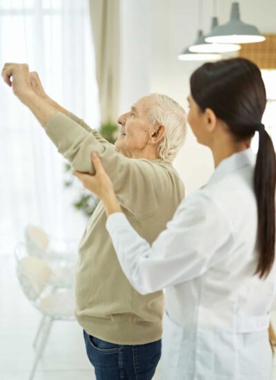 Female doctor helping an elderly man to do exercises in room